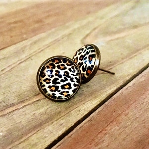 May include: A pair of gold-toned stud earrings with a leopard print design. The earrings are round and have a glossy finish.