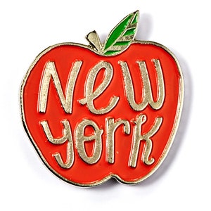 May include: A red apple pin with a gold outline and the words "New York" in gold lettering.
