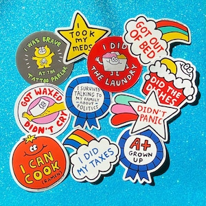 May include: A selection of brightly coloured, die-cut stickers featuring amusing phrases and illustrations. Designs include a star that says "I took my meds," a cloud with a rainbow that says "I did my taxes," and a badge that says "A+ Grown Up."