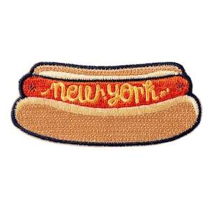 May include: Embroidered patch in the shape of a hot dog. The hot dog has a red sausage, yellow mustard, and a tan bun. The words "New York" are embroidered in yellow cursive across the hot dog.