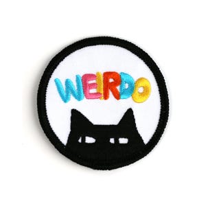 May include: Round embroidered patch with a black border. The patch features the word "WEIRDO" in colorful, embroidered letters above a black cat silhouette with white eyes. The background is white.