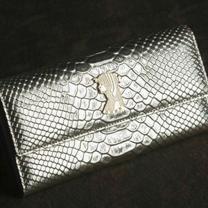 May include: A silver snakeskin wallet with a gold-toned embossed design.