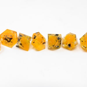 May include: Six yellow and black dice with a speckled, translucent finish. The dice are arranged in a row on a white surface.