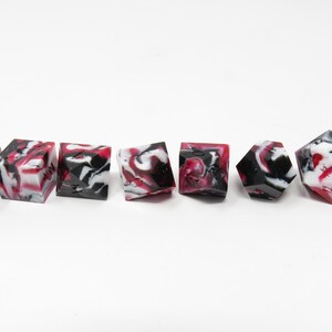 May include: Set of seven red, white, and black marbled dice. The dice are polyhedral and have black numbers.