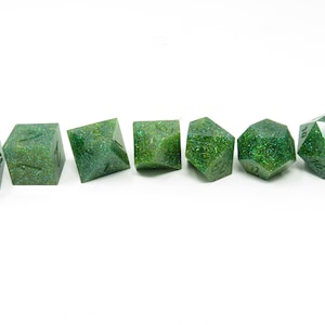 May include: Set of seven green glitter dice with black numbers. The dice are a d4, d6, d8, d10, d%, d12, and d20.