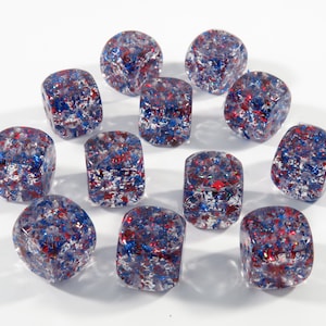 Könnte beinhalten: Zwölf transparente Würfel mit rotem, blauem und silbernem Glitzer im Inneren. Die Würfel sind in einem Kreis auf weißem Hintergrund angeordnet.