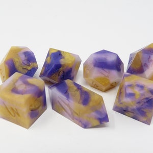 May include: Set of seven purple and gold dice with white swirl patterns. The dice are made of resin and have a glossy finish.