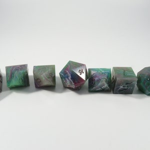 May include: Set of seven polyhedral dice with a green, pink, and white marbled pattern. The dice are numbered 1 through 6 and 16.