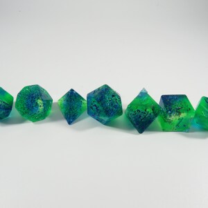 May include: Set of seven green and blue dice with glitter embedded in the resin. The dice are various shapes, including a d4, d6, d8, d10, d12, and two d20s.