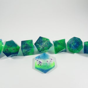 May include: Set of seven green, blue, and white dice with glitter embedded in the resin. The dice are translucent and have a swirling pattern.