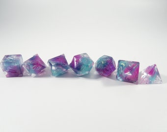 May include: Set of seven iridescent dice with pink, blue, and white swirls. The dice are translucent and have white numbers.