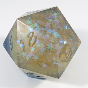 Op de afbeelding: Een lichtbruine, iriserende, veelzijdige dobbelsteen met een sterpatroon en de nummers 1, 2, 3, 4, 5, 6 en een schedel op de zijden.
