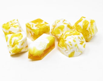 May include: A set of six yellow and white marbled dice. The dice are made of resin and have a swirl pattern.