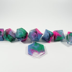 May include: A collection of polyhedral dice in various shapes, featuring a translucent design with swirls of blue, green, and pink. The dice are arranged on a white surface, showcasing their colorful, marbled appearance.
