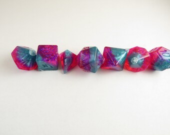 May include: Set of seven iridescent dice with pink and blue swirls and glitter. The dice are made of resin and have a clear finish.