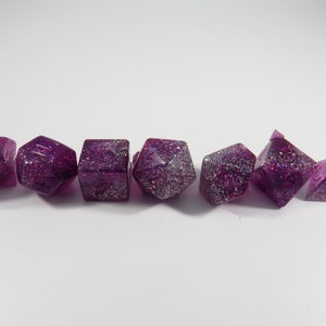 Peut inclure: Ensemble de sept dés à jouer en paillettes violettes et argentées avec différents numéros sur chaque face.