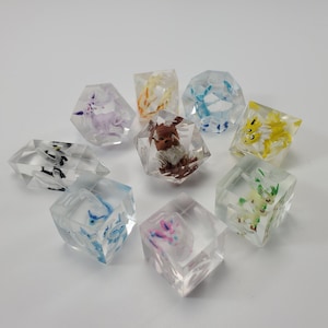 Könnte beinhalten: Neun transparente Würfel mit verschiedenen Pokémon-Charakteren darin. Die Würfel sind in verschiedenen Farben, darunter rosa, blau, gelb und braun.