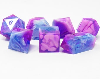 May include: Set of six iridescent dice with a swirling blue and purple color scheme. The dice are made of clear resin with pink and white swirls and glitter.