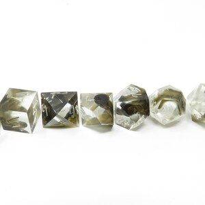 May include: Set of seven clear dice with black and white markings. The dice are translucent and have a speckled appearance. The dice are arranged in a row on a white background.