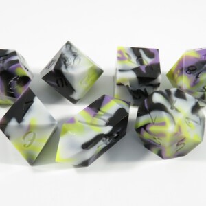 以下が含まれることがあります： 黒、白、紫、黄色のマーブル模様のサイコロ6個セット。サイコロは1から6まで番号が振られています。