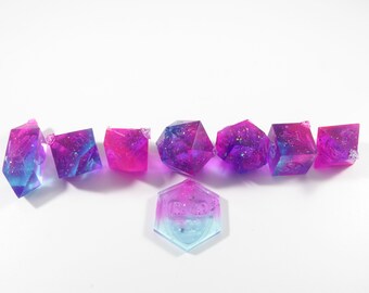 May include: Set of eight iridescent dice with a blue and pink gradient. The dice are made of clear resin with glitter embedded in the resin. The dice are in the shape of a cube, a d4, a d6, a d8, a d10, a d12, and a d20.