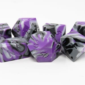 Könnte beinhalten: Ein Satz von sechs violetten, schwarzen und weißen Würfeln mit wirbelnden Mustern. Die Würfel sind aus einem durchsichtigen Material gefertigt und haben schwarze Zahlen.