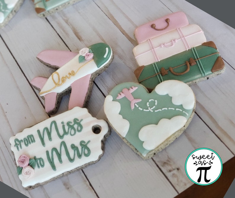 May include: A set of six decorated cookies featuring a heart-shaped cookie with a plane flying over clouds, a tag cookie with the text "from Miss to Mrs", a plane cookie with the text "love", and three stacked luggage cookies. The cookies are decorated with green, pink, and white icing.
