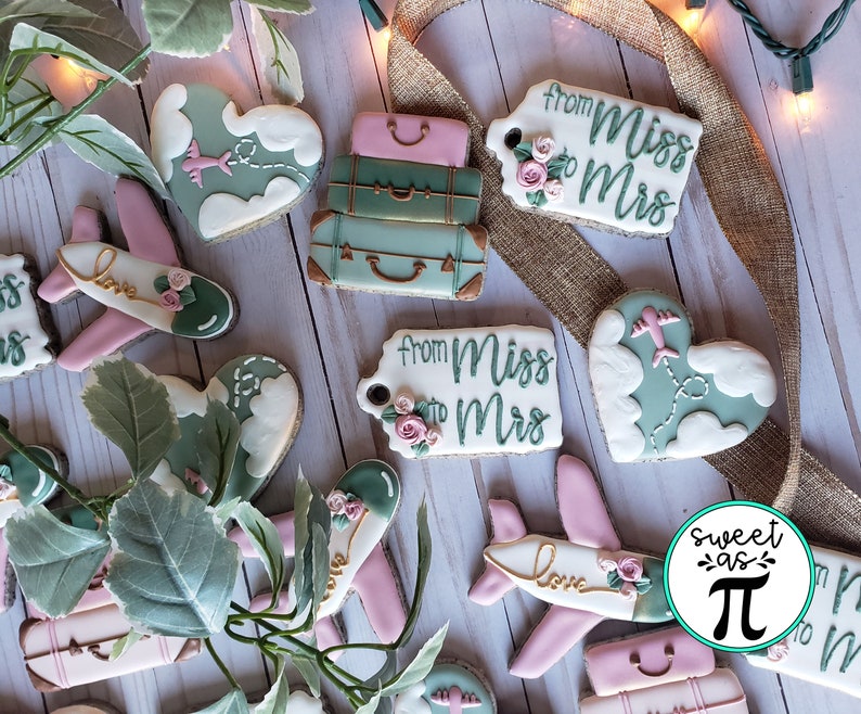 May include: Assortment of decorated sugar cookies with travel themes. Cookies feature airplanes, luggage, hearts, and tags with the text "From Miss to Mrs".