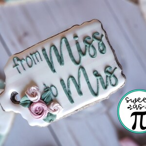 May include: A white cookie decorated with green icing that reads "from Miss to Mrs." and features a floral design with pink and green icing.