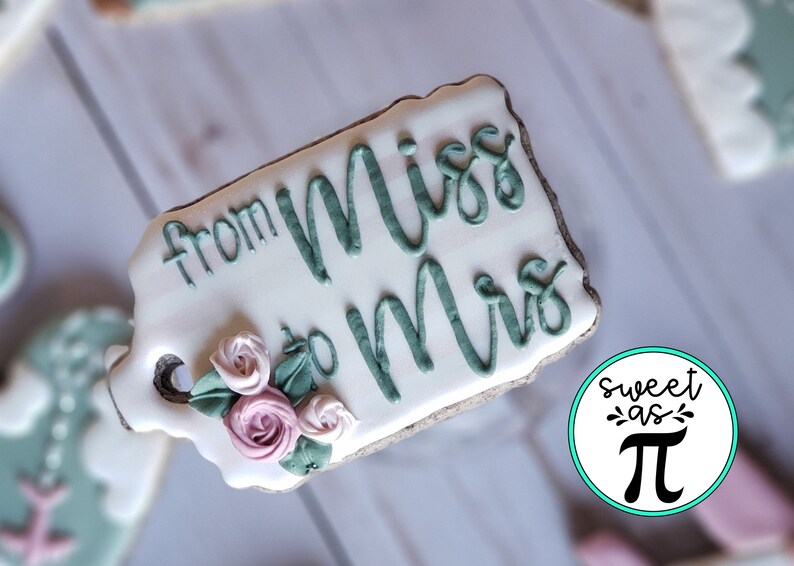 May include: A white cookie decorated with green icing that reads "from Miss to Mrs." and features a floral design with pink and green icing.