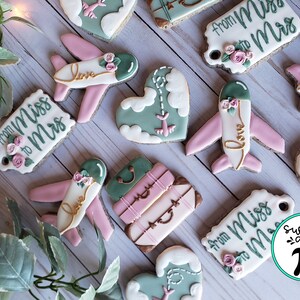 May include: A set of decorated cookies with a travel theme. The cookies feature airplanes, luggage, hearts, and the text "from Miss to Mrs".