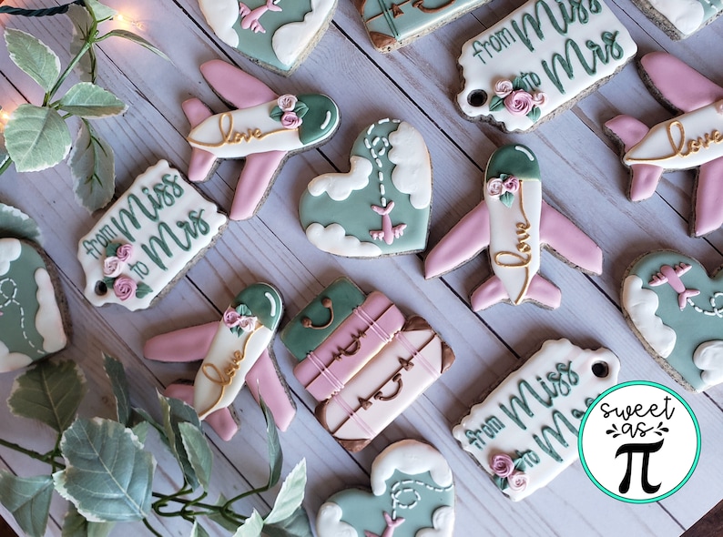 May include: A set of decorated cookies with a travel theme. The cookies feature airplanes, luggage, hearts, and the text "from Miss to Mrs".