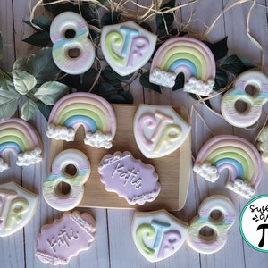 May include: A collection of decorated sugar cookies featuring rainbows, the number 8, and the initials CTR. Some cookies also have the name Katie written on them. The cookies are arranged on a wooden surface. The text "Sweet as Pi" is visible in the lower right corner of the image.