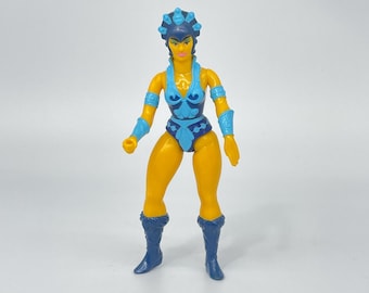 May include: A yellow plastic action figure of a female warrior wearing blue and white clothing, a blue crown, and blue boots.