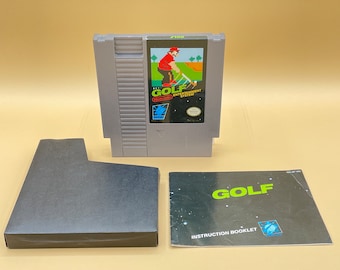 May include: A Nintendo Entertainment System (NES) game cartridge for the game "Golf" with a gray plastic case and a black label with white text. The game cartridge is accompanied by a black instruction booklet with a white label and the text "GOLF" in green letters.