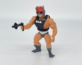 May include: A vintage action figure of a muscular character in a red helmet and black armor, holding a black weapon. The figure is tan with gray boots and underwear. The armor has a white "E" on the chest.