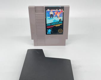 May include: A gray Nintendo Entertainment System (NES) game cartridge labeled "PRO WRESTLING" with a colorful graphic of wrestlers. A black, rectangular base sits below the cartridge.