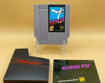 May include: A gray Nintendo Entertainment System (NES) video game cartridge for Kung Fu, with a blue and white label. The game is displayed with its black box and instruction booklet. The box has the Nintendo logo in red.
