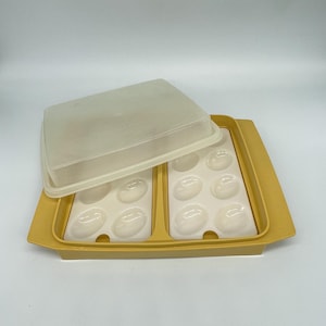 May include: A vintage yellow plastic egg container with a clear lid. The container has two sections, each holding six egg-shaped indentations. The lid is slightly ajar, revealing the interior.