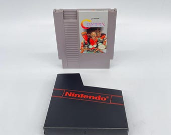 May include: A gray Nintendo Entertainment System (NES) game cartridge with the game title "Contra" on the label. The black game box with the Nintendo logo is below the cartridge.