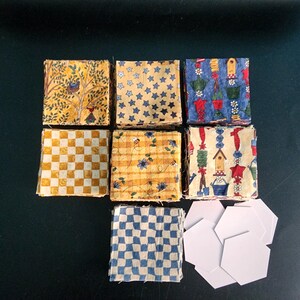 May include: A collection of fabric squares featuring various patterns including yellow trees, blue stars, garden motifs, yellow and white checkers, floral prints, and blue and white checkers, accompanied by several white paper hexagon templates.
