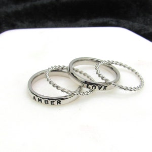 May include: Three silver rings, one with the word "LOVE" engraved on it, another with the word "AMBER" engraved on it, and a third with a twisted rope design.