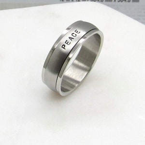 May include: A silver stainless steel ring with a beveled edge and the word "PEACE" engraved on the band.