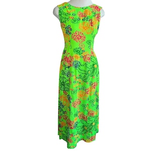 May include: A sleeveless, floor-length dress in a vibrant neon green hue. The dress is adorned with a colorful floral pattern featuring orange, red, and blue accents. The dress has a scoop neckline and a straight silhouette, perfect for a retro look.