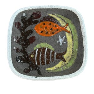 May include: Square ceramic dish with a dark gray background and a white border. The dish features an orange fish with black spots, a brown and white striped fish, a white starfish, and green and yellow seaweed.