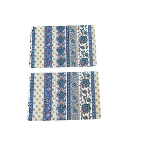 May include: Two rectangular fabric placemats with a repeating pattern of vertical stripes. The stripes alternate between floral designs, solid blue, and a cream-colored background with small blue and yellow floral accents. The placemats are likely for dining.
