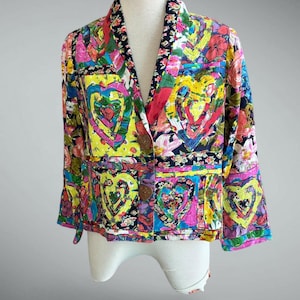 May include: A long-sleeve blazer featuring a vibrant patchwork design with colorful heart motifs, floral patterns, and geometric shapes. The jacket has a notched lapel, two large brown buttons for closure, and a structured fit.