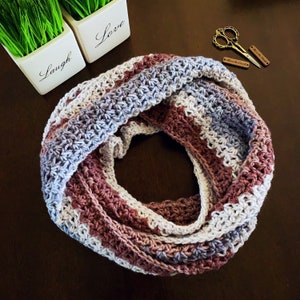 May include: A crocheted infinity scarf with a multi-colored striped pattern in shades of purple, pink, and white.