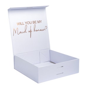 May include: A white gift box with a lid that is open. The lid has the words "Will you be my Maid of honour?" printed in gold foil.