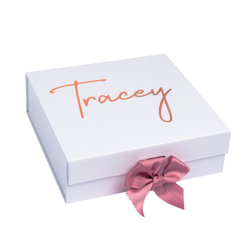 May include: White gift box with a pink ribbon and the name "Tracey" written in gold lettering on the top.